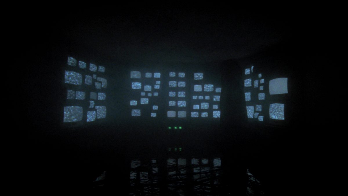 Figure before a wall of static monitors